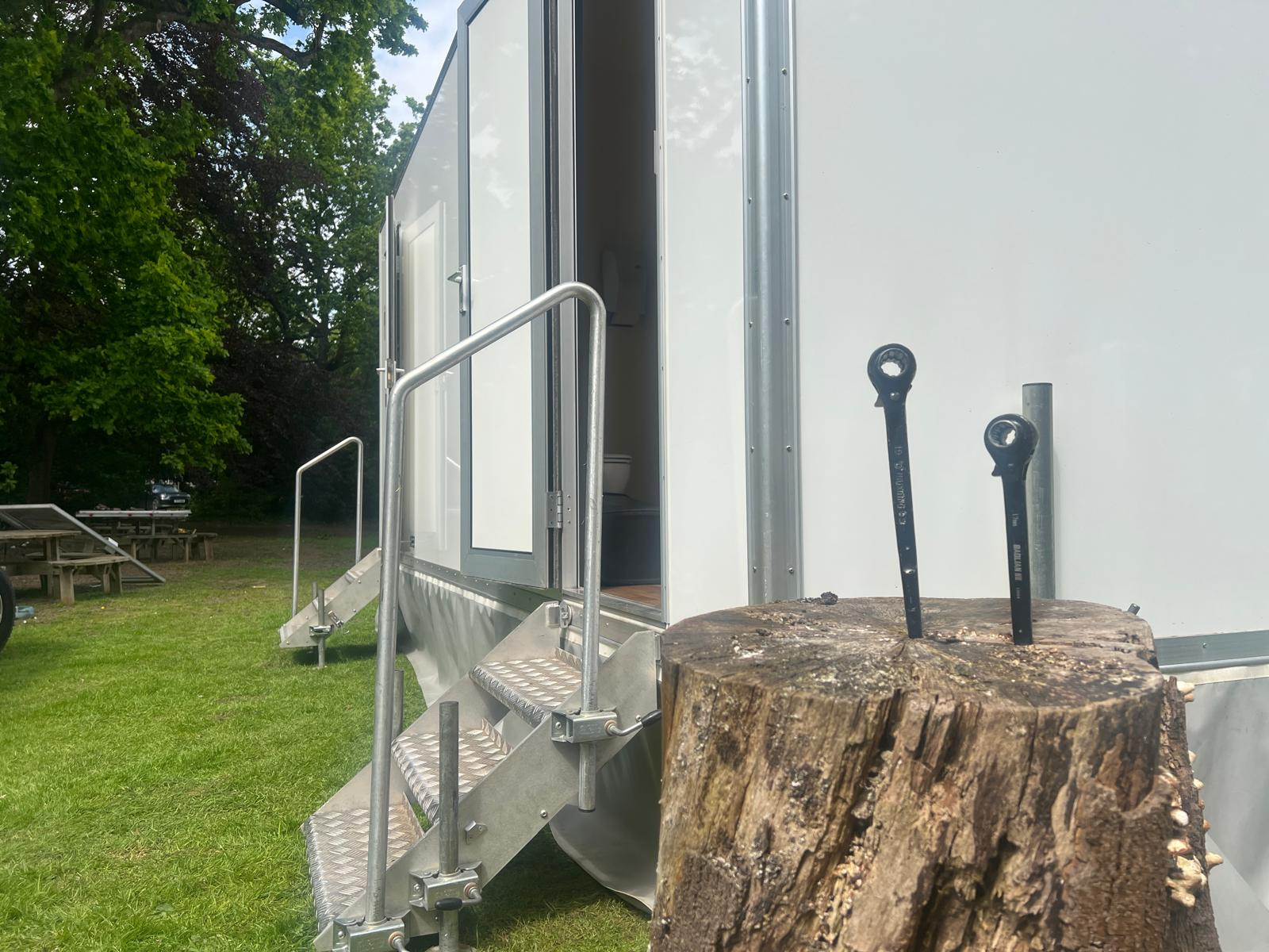 Luxury toilet trailer with open door and aluminium entrance steps set up on grass at an outdoor event